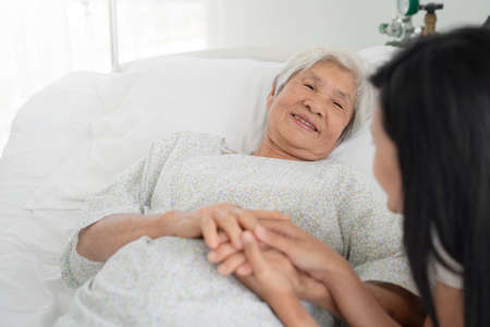 close up of patient grandfather and women holding hands in hospital bedの写真素材