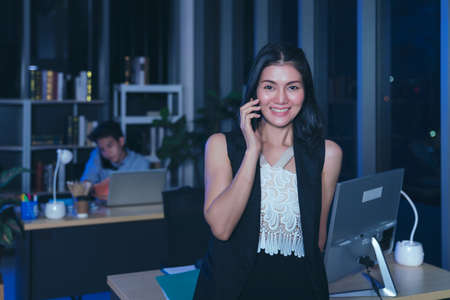Businesspeople in the office at night working late, coffee and  calling phone working overtime together over a laptop at a desk in an office in the late eveningの写真素材