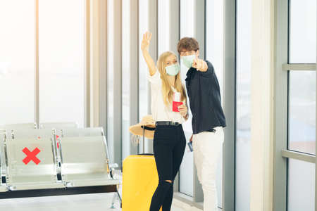 portrait of young traveler in protective mask holds passport during affected by flight delay and cancelled travel and vacation. Travel ban due to coronavirus outbreak and covid-19 ncov virus epidemicの写真素材