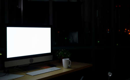 Room illuminated by a computer screen at night, no people,  Empty workplace place in the office at night with a city view from windowの写真素材