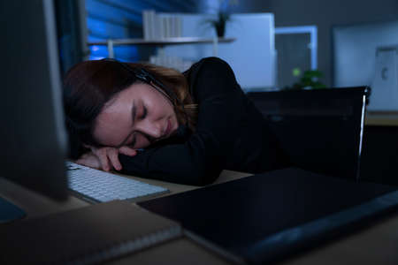 Thai asian women call center business people get headache and migraine from working late night shift for helping assistance customer in workplace at night timeの写真素材