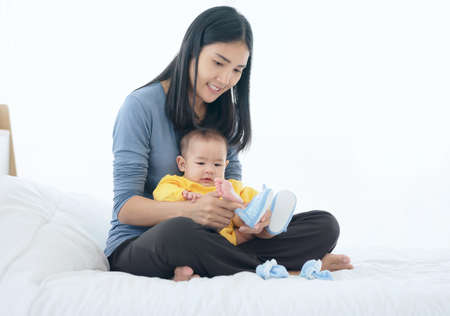 Loving mother putting shoes on baby on sofa at homeの写真素材
