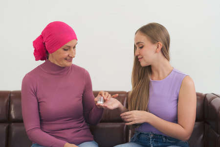 Young adult female cancer patient spending time with her daughter at home. Take medicine family support concept.の写真素材