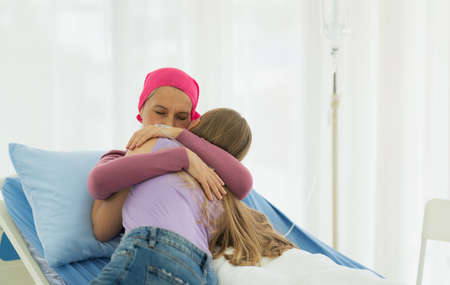 Young adult female cancer patient spending time with hug her daughter on bed at hospital. family support concept.の写真素材
