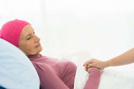 Cancer woman lying supported by mum at home. trust and ethics conceptの写真素材