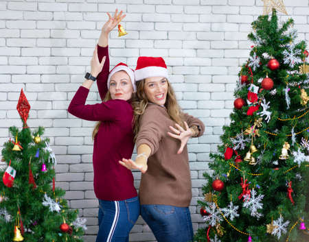 Smiling beautiful woman dancing around a decorated Christmas tree, before New Year eve at home,...