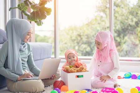 Muslim Mother working with laptop and Cute little baby playing toys in living room at home.の写真素材