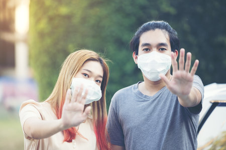 Young asia couple in protective masks showing stop gesture at garden homeの写真素材