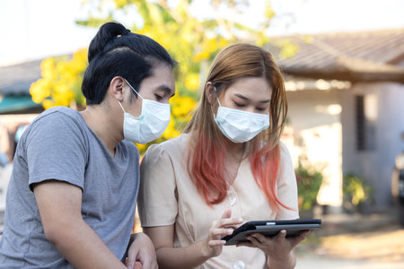Young asia couple using smart mobile phote outdoor wearing face mask during coronavirus outbreak - Millennial couple watching videos on smartphone - Social distance and technology conceptの写真素材