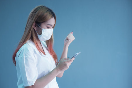 Young woman wearing mask using smartphone over isolated background very happy pointing with handの写真素材