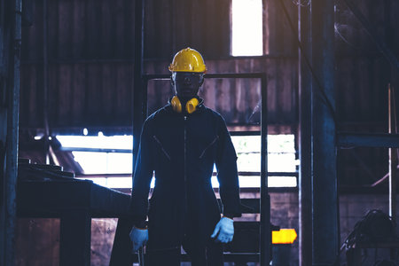 Portrait worker man with yellow helmet and ear protection in factory, Dark toneの写真素材