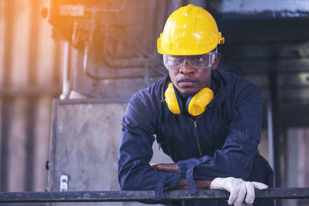 Portrait worker man with yellow helmet and ear protection in factory, Dark tone