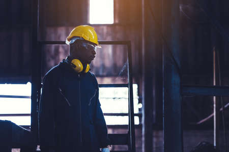 Portrait worker man with yellow helmet and ear protection in factory, Dark toneの写真素材