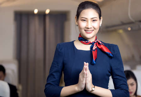 Asian flight attendant posing with smile at middle of the aisle inside aircraft passenger seat on the backgroundの写真素材