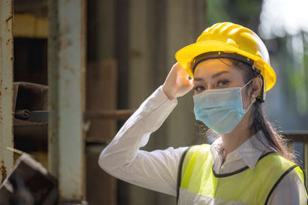 A portrait of an industrial woman engineer with mask standing in a factory. Work at the Heavy Industry Manufacturing Facility concept.の写真素材