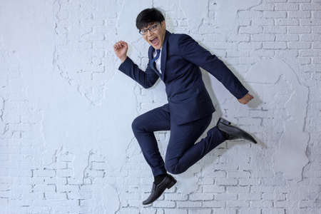 Funny cheerful businessman jumping in air over white wall backgroundの写真素材