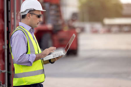 Confident Caucasian man engineer wearing white safety helmet using computer laptop and check for...