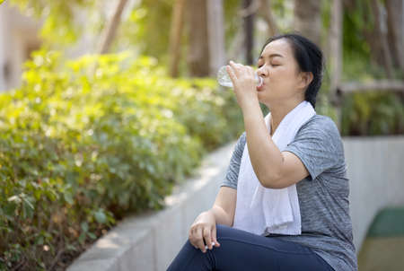 Senior athletic woman drinks water from a bottle after running in the park.の写真素材