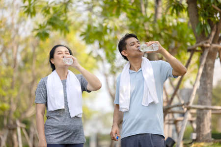 Senior people, old man and woman talking and drinking water after exercising in parkの写真素材