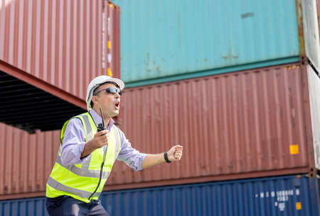 Man Using Walkie Talkie At Container Terminal, Industrial worker is controlling container loading