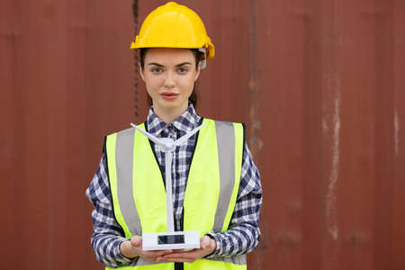 factory workers or engineers holding light bulb and using tablet computer with windmill model on solar panel,  work in containers warehouse storageの写真素材