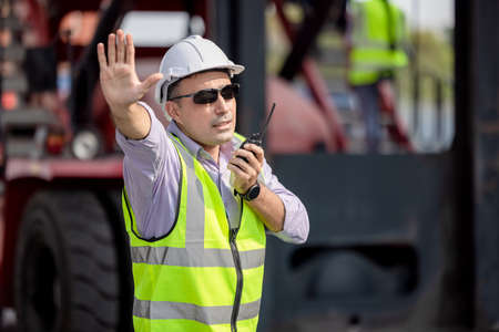 Man Using Walkie Talkie At Container Terminal, Industrial worker is controlling container loadingの写真素材
