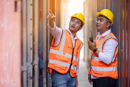 Two factory workers or engineers looking and pointing something in containers warehouse storageの写真素材