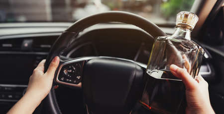 Driver is driving a car with a bottle of whisky in hand. Drunk driving concept.の写真素材