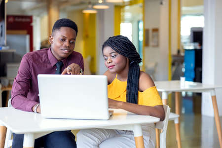 Portrait of two black students with netbook sitting at home interior, african american using laptop computer for searching information and making bookingの写真素材