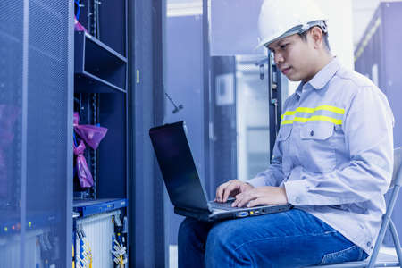 Network administrator holding laptop in hand working Configuration with core switch on rack cabinet...