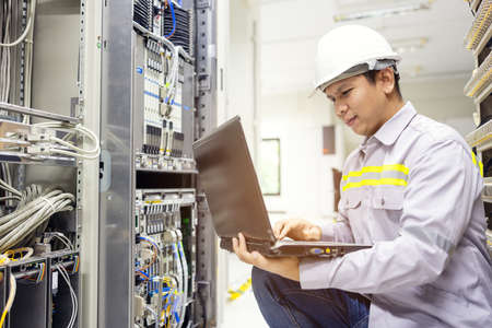 Network administrator holding laptop in hand working Configuration with core switch on rack cabinet...