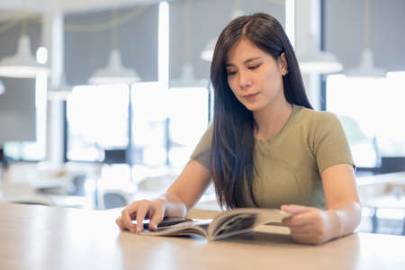 Positive woman indoors sitting at library reading book or magazine.の写真素材