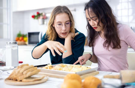 Beautiful baker making pastries, Cute happy two Women have fun a bread making classroom and use their hands to slap the dough together to make cakes together in the home kitchen.の写真素材