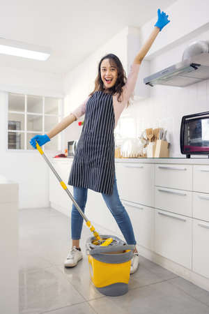 Portrait of cheerful young housewife holding cleaning supplies, smiling and looking at camera in...