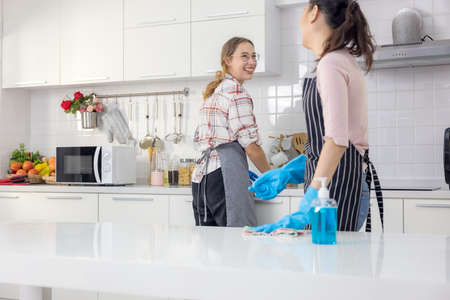 Portrait of cheerful young housewife holding cleaning supplies, smiling and looking at camera in kitchen. Professional cleaning service specialist offering help with domestic dutiesの写真素材