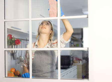 Happy woman in gloves cleaning  the glass window at home kitchen. Housework concept.