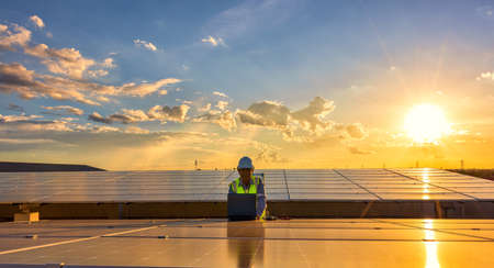 Engineer using laptop at solar panels on rooftop at sunset sky, An engineer working at a...