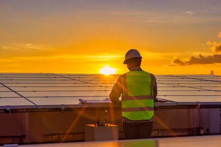 Engineer using laptop at solar panels on rooftop at sunset sky, An engineer working at a photovoltaic farm. Eco technology for electric powerの写真素材