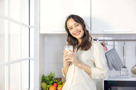 In a light modern kitchen, a beautiful woman drinks milk while listening to music. Before breakfast,...