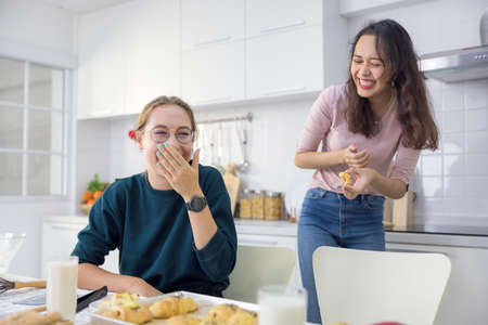 Cute happy two, beautiful baker baking sweets Women had a good time in a bread-making lesson and use their hands to slap dough together in the kitchen to make cakes together.の写真素材