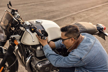 On the route to a summer vacation on a motorcycle, Biker guy On an asphalt highway, a crouching motorcyclist is concerned about a motorcycle breakdown.の写真素材