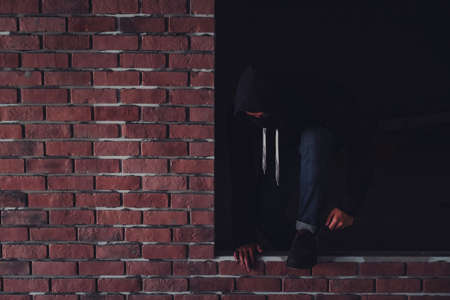 A burglar dressed in dark and wearing a leather coat smashes a window at a residence.
