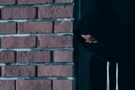 A burglar dressed in dark and wearing a leather coat smashes a window at a residence.