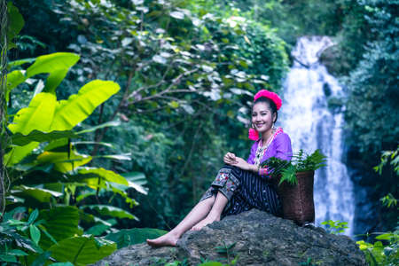 At a river waterfall in the Thai countryside, a young woman wears a flower crown on a rock.