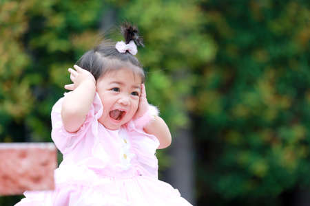 Sitting on the green grass, a lovely little girl wears pink fashionable clothing.の写真素材