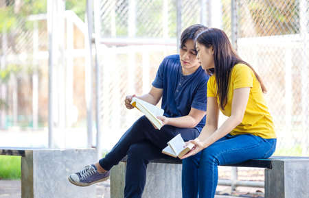 On a campus, a couple of students are studying together, and a teenager sits on a seat beside a sports court with a book.の写真素材