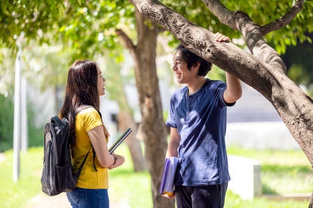 A couple of Thai high school students smile while going through the woods with a book in their hands, guy and girl outdoors.の写真素材