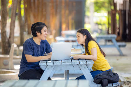 At the public park, a happy young couple using a laptop sits at a table.の写真素材
