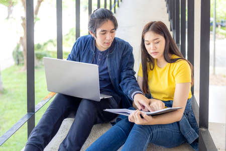 In the university campus, two Asian couples sit on the stairwell with their thumbs up, working on...