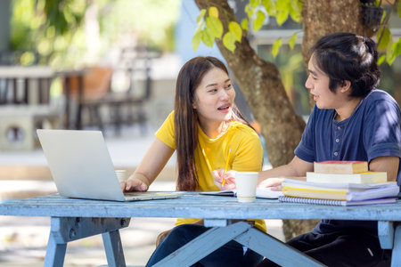 Couple Of Students Sitting And Using Laptop In Outdoor University Doing Some Online Research